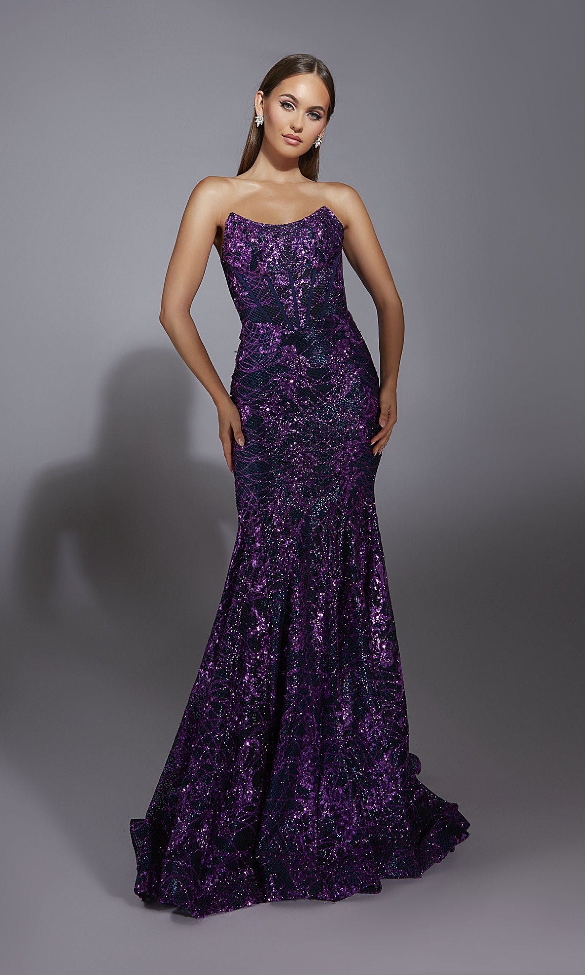 A woman poses in the Alyce 61887 long prom dress, a strapless, floor-length purple sequin mermaid gown with shimmering embellishments, beautifully standing out against a plain gray background.