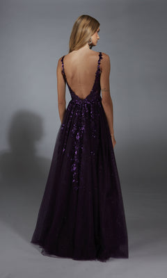 A woman faces away, wearing the Alyce 61891 long prom dress featuring a dark purple hue, deep low-cut back, sequin accents, and an elegant A-line glitter tulle skirt.