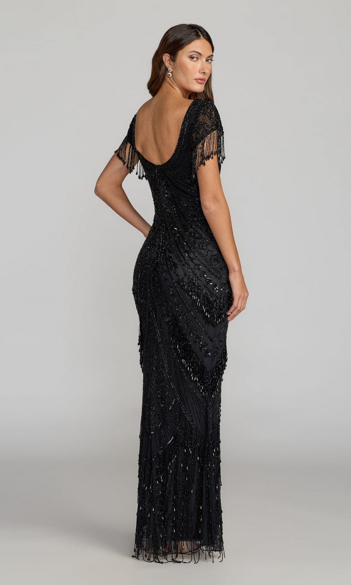 A woman, seen from behind, wears the Long Formal Dress: Mac Duggal 6190—a black, floor-length beaded evening gown featuring fringe details, short sleeves, and a low scoop back—while standing against a plain light background.