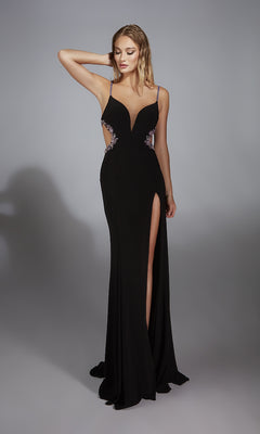A woman models the Alyce 61902 long prom dress—floor-length, black, with a thigh-high slit and decorative cutouts—against a plain gray background.