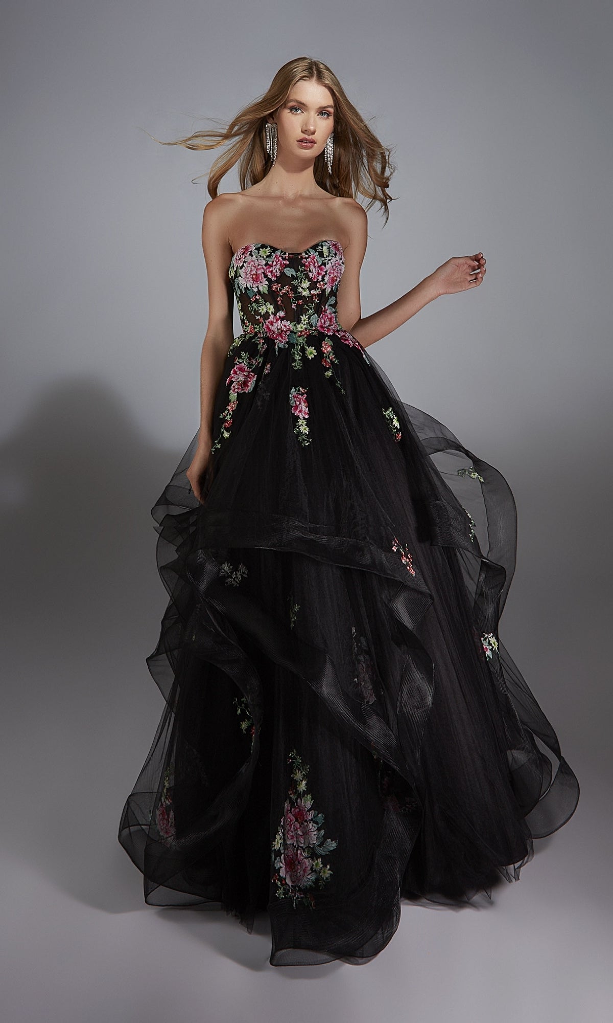 A woman poses against a plain gray background in the Alyce 61914 long prom dress, featuring a strapless design, pink and green floral embroidery, and a flowing tulle skirt.
