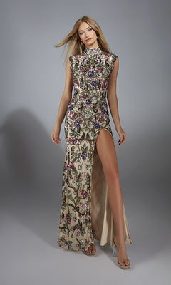 A woman stands against a plain gray background wearing the Alyce 61918 long prom dress, featuring a sleeveless high-neck design, floral sequin embroidery, and a high leg slit.
