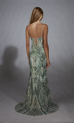 A woman with long blonde hair models the Alyce 61920 long prom dress, a green and silver sequin gown with a lace-up back, standing with her back to the camera against a plain gray background.