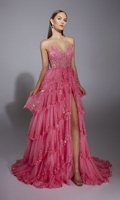 A woman stands against a plain gray background wearing the Alyce 61927 long prom dress: a tiered, bright pink sleeveless gown with a sheer corset bodice, floral embellishments, and a high slit.