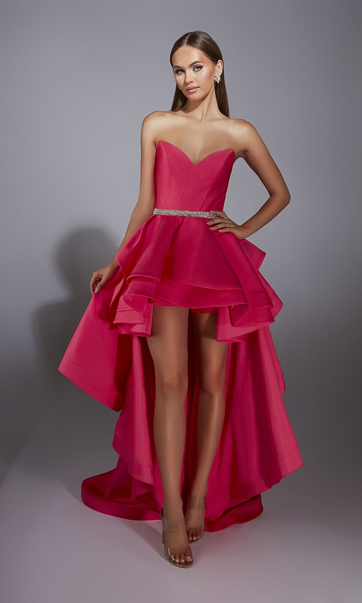 A woman poses confidently against a plain gray background in the Alyce 61934 High-Low Strapless Prom Dress, featuring a bright pink mikado fabric, a layered A-line skirt, and a beaded waistline.