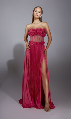 A woman models the Alyce 61935 long prom dress—pink, strapless, with 3D flower detail on the bodice, a pleated skirt, and a thigh-high slit—standing before a plain gray background.