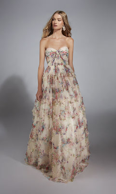 A woman wears the Alyce 61957 long prom dress, featuring a strapless floral design with a corset bodice and flowing A-line skirt, standing against a plain gray background.