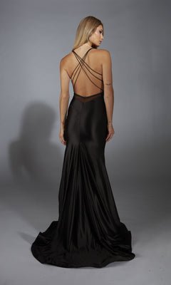 Woman wearing Alyce 61966, a black satin long prom dress with a v-neckline and thin crisscross straps, stands facing away against a plain gray background.