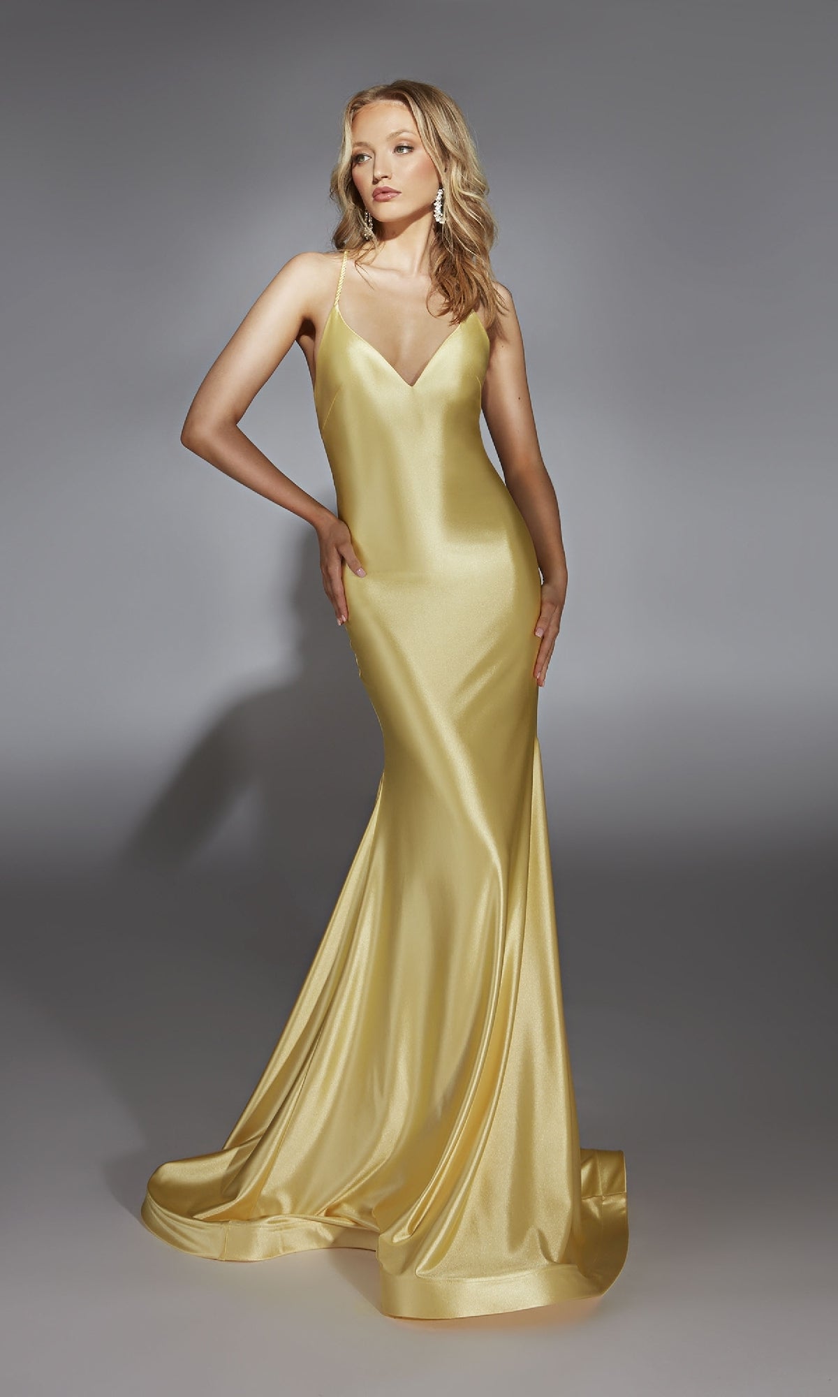 Woman wearing the Alyce 61966 long prom dress—sleeveless, floor-length gold satin with a fitted bodice, v-neckline, and flowing skirt—stands against a plain gray background.