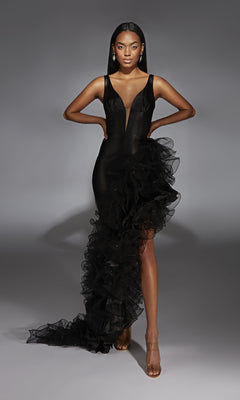 A woman poses with hands on hips in the Alyce 61967, a fitted long black prom dress crafted from stretch satin, featuring a sheer plunging neckline and dramatic one-sided floor-length ruffle.