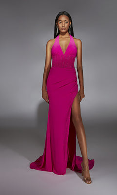Woman in a studio wearing the Alyce 61968 long prom dress—a sleeveless, floor-length magenta gown with a high slit, corset bodice, and embellished waist—paired with clear heeled sandals.