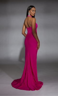 A woman faces away, wearing the Alyce 61968 Long Prom Dress—a fitted magenta gown with a corset bodice and flowing train—paired with statement earrings against a gray backdrop.