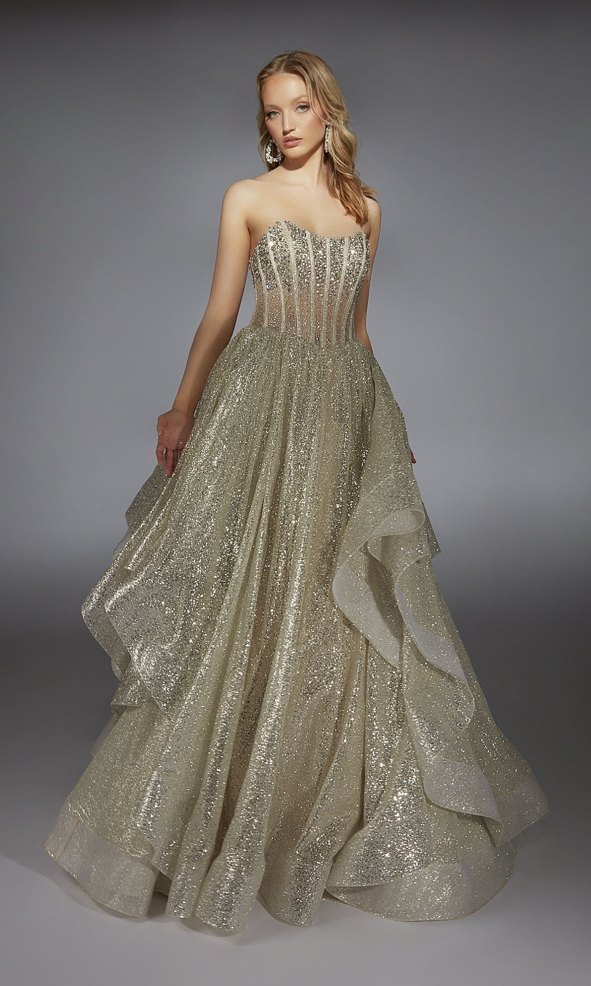 A woman in the Alyce 61971 long prom dress, featuring a beaded corset bodice and layered ruffled skirt, stands against a plain gray background.