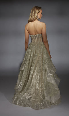 A woman faces away wearing the Long Prom Dress: Alyce 61971, a designer ball gown with a strapless beaded corset bodice and layered glitter skirt, set against a plain gray background.