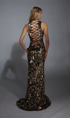 A woman faces away, wearing the Alyce 61975 long prom dress—a black and gold sequin gown with a floral pattern and strappy open back—posed against a plain gray background.