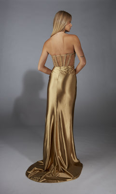 A woman faces away, modeling the Alyce 61976 long prom dress. The strapless gown has a fitted, semi-sheer sequin corset and a flowing gold skirt, shown against a plain gray background.