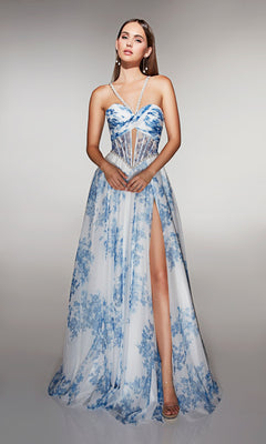 A woman models the Alyce 61994, a long prom dress with white and blue floral print, thin straps, corset bodice, and high leg slit. Her straight brown hair falls gracefully as she poses before a plain backdrop.