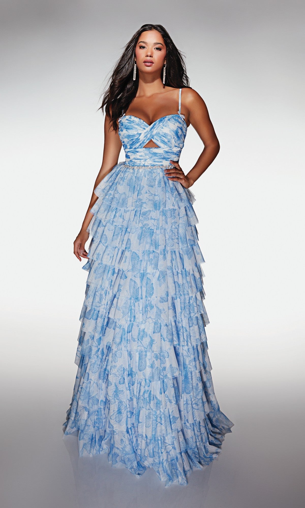 A woman stands against a gradient background wearing the Alyce 62018 long prom dress—a sleeveless, floor-length light blue gown featuring ruffles and a midriff cutout.