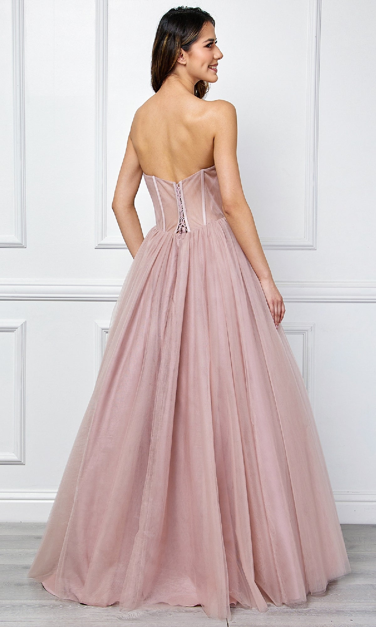 Woman modeling the back of a dusty rose pink ball gown in front of a white wall.