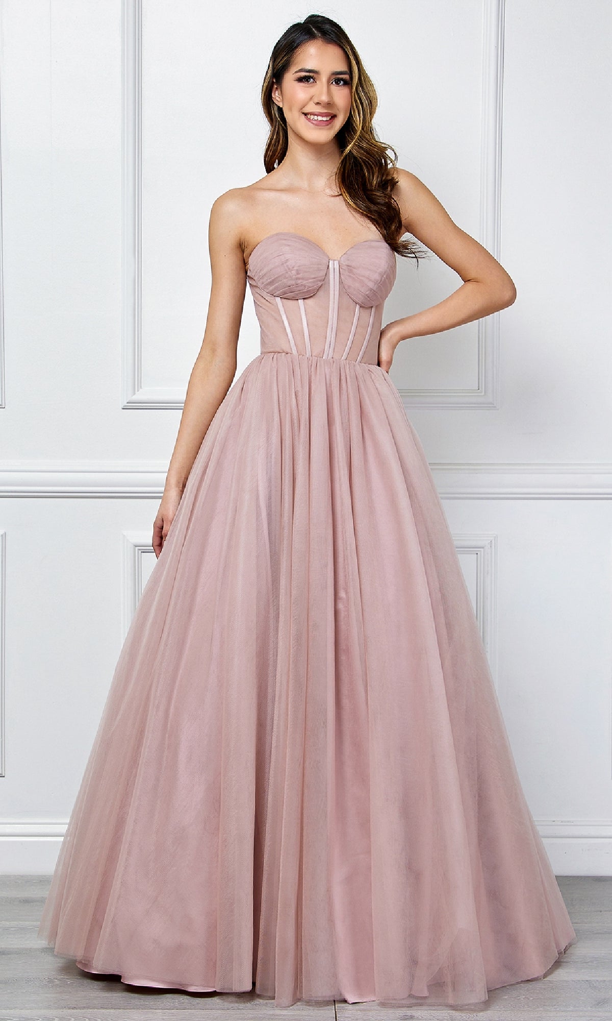 Woman wearing a strapless pink ball gown against a white wall