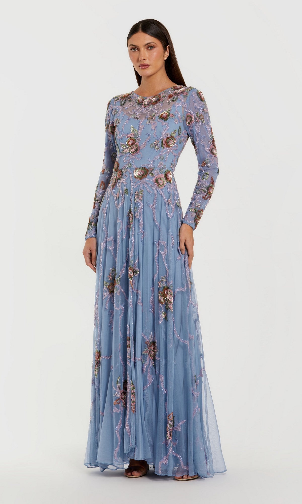 A woman stands against a plain white background wearing the Mac Duggal 6202—a long, slate blue formal dress featuring long sleeves and intricate floral embroidery.