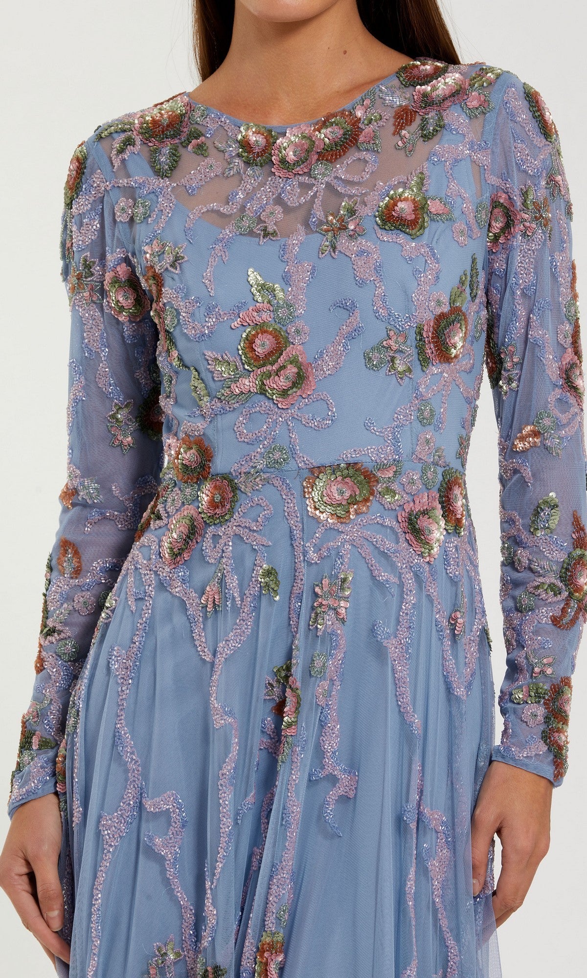 A woman models the Mac Duggal 6202 Long Formal Dress—a sheer, blue, long-sleeve gown adorned with intricate floral embroidery and beading—shown from shoulders to mid-thigh.