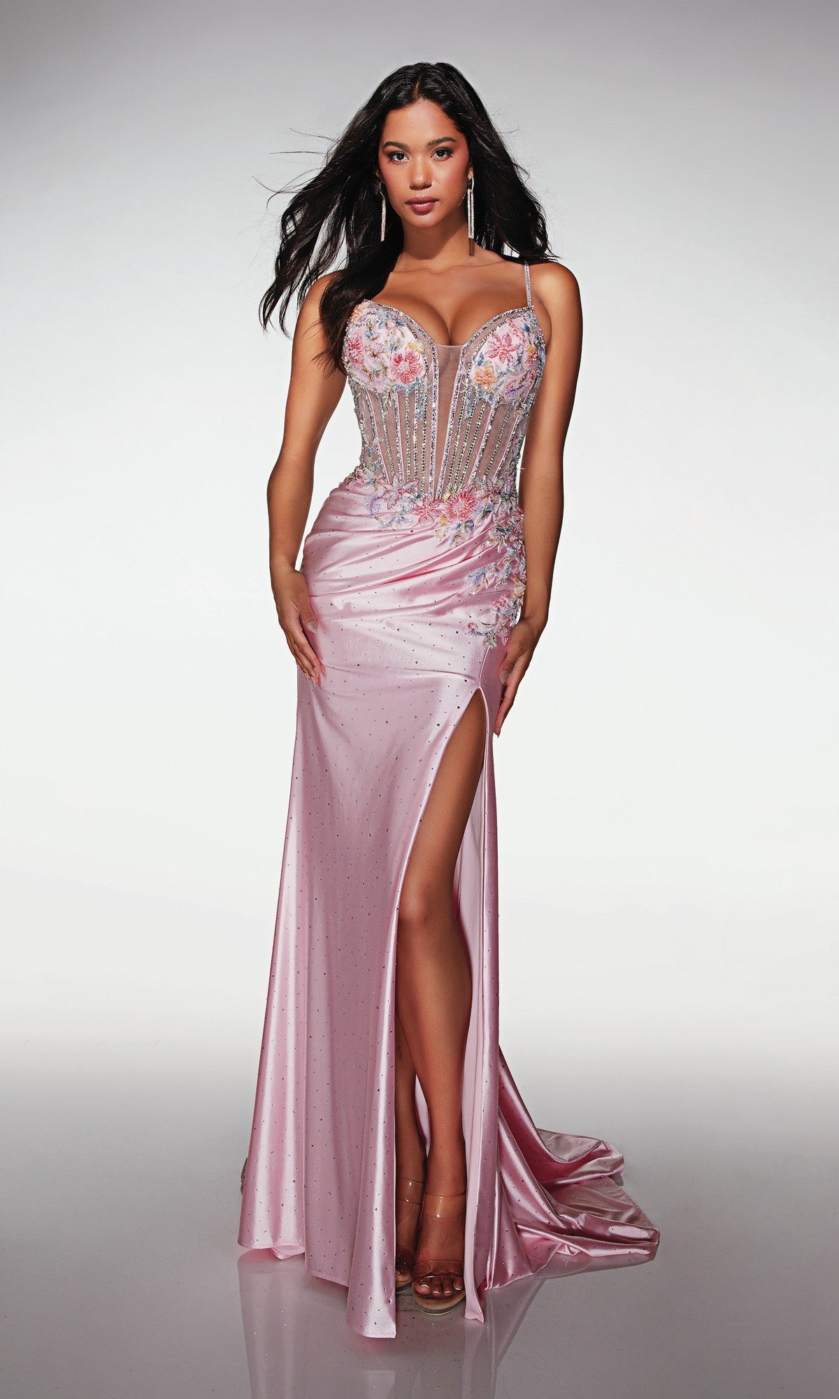 Woman wears the Alyce 62022 long prom dress in Rosewater, featuring a fitted, sleeveless design with a high-leg slit, floral embellishments, and beaded corset bodice, posing against a plain background.