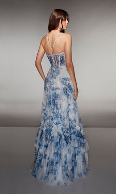 A woman faces away, wearing the Alyce 62028 long prom dress featuring blue-and-white floral print, thin straps, a sheer corset bodice, and tiered layers against a neutral background.