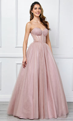 A woman models the Amelia Couture 6202 Strapless Corset Prom Ball Gown—a blush pink tulle dress with a fitted bodice and full skirt—standing indoors against a white paneled wall.