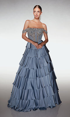 A woman wearing the Alyce 62035 Long Prom Dress, with an off-the-shoulder blue beaded corset bodice and satin tiered skirt, stands against a neutral background.