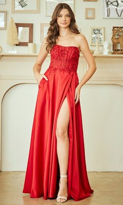 Woman wearing the Amelia Couture 6204 long prom dress, featuring a strapless beaded bodice and thigh-high slit, standing indoors before a decorated mantel.