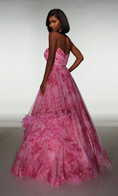 A woman poses with her back partially turned, wearing the Alyce 62042 long prom dress—a strapless pink floral ballgown featuring a ruffle skirt and 3D flower details—against a plain background.