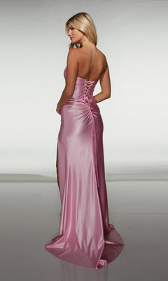A woman wearing the Alyce 62046 long prom dress—strapless, floor-length pink satin with a fitted corset bodice and lace-up back—stands facing away from the camera.