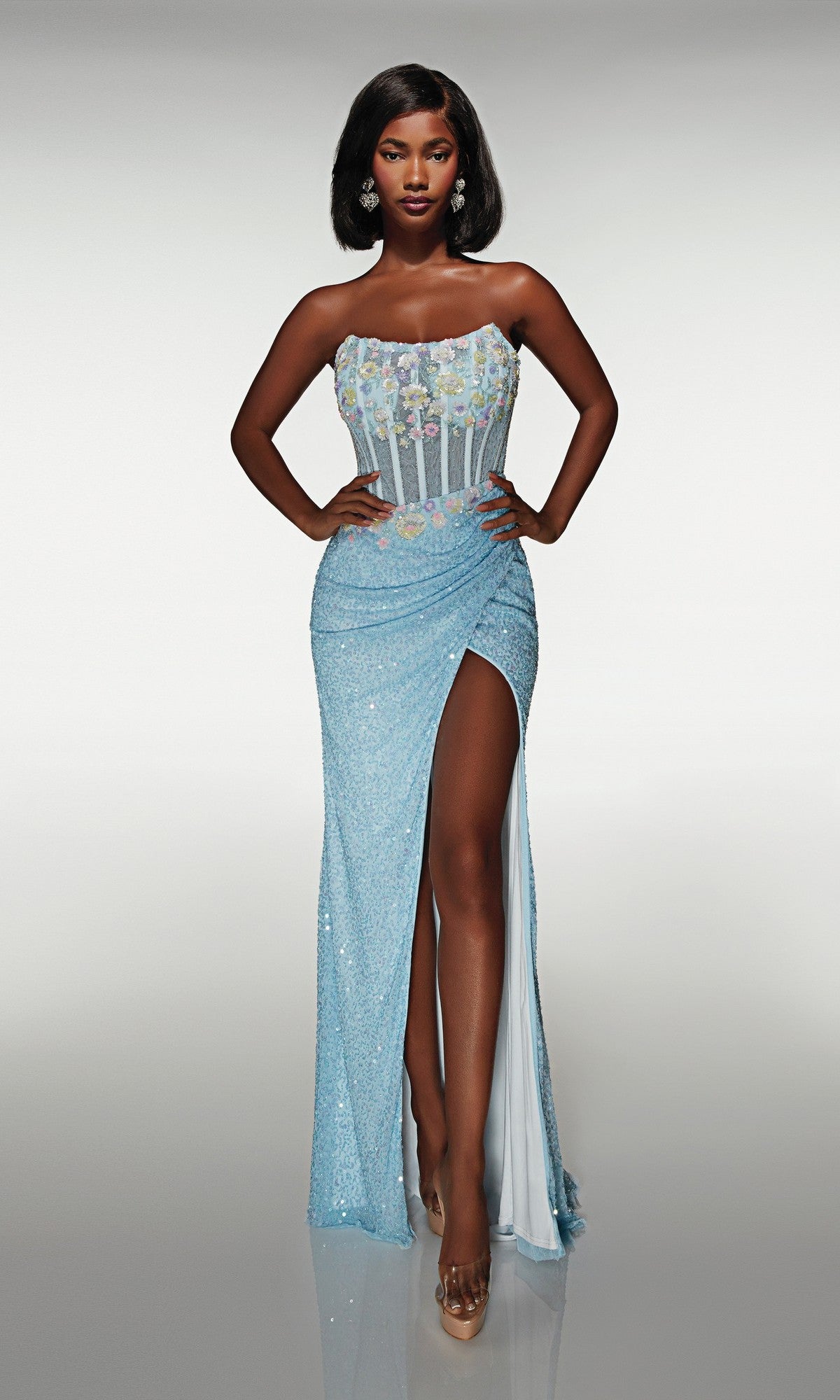 A woman poses against a plain background in the Alyce 62047 long prom dress, featuring a blue strapless design with floral appliques on the bodice, a thigh-high slit, and nude heels.