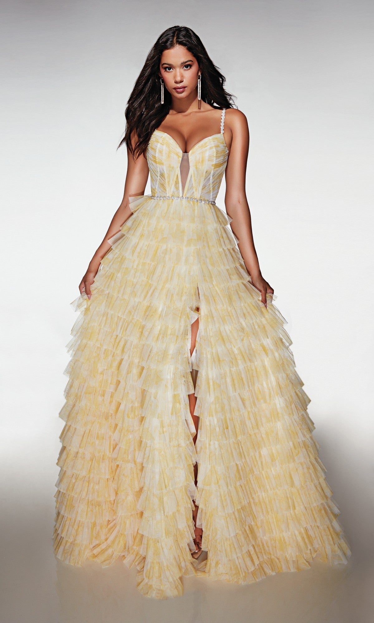 A woman wears the Alyce 62052 long yellow prom dress with a corset bodice, thin straps, and a ruffled A-line skirt with front slit, standing against a plain background.