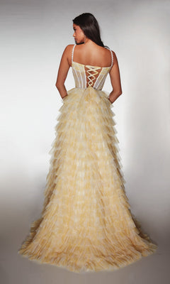 A woman wearing the Alyce 62052 long prom dress in light yellow, featuring a tiered ruffle skirt and fitted lace-up bodice, stands with her back to a plain background.