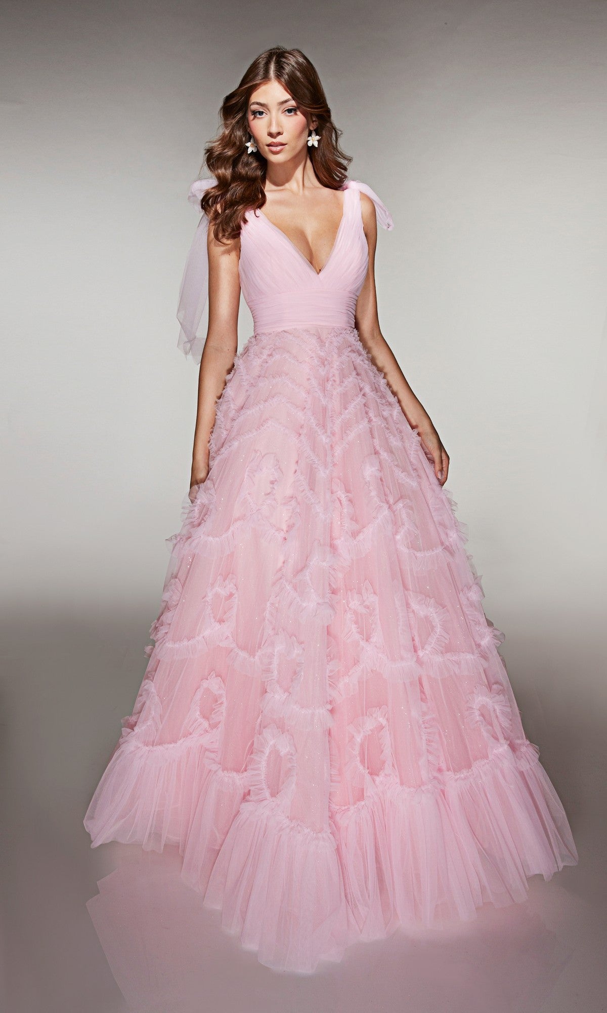 A woman in the Alyce 62079 long pink tulle prom dress, featuring a ruffled A-line skirt, deep V-neckline, and ribbon shoulder straps, stands against a neutral background.