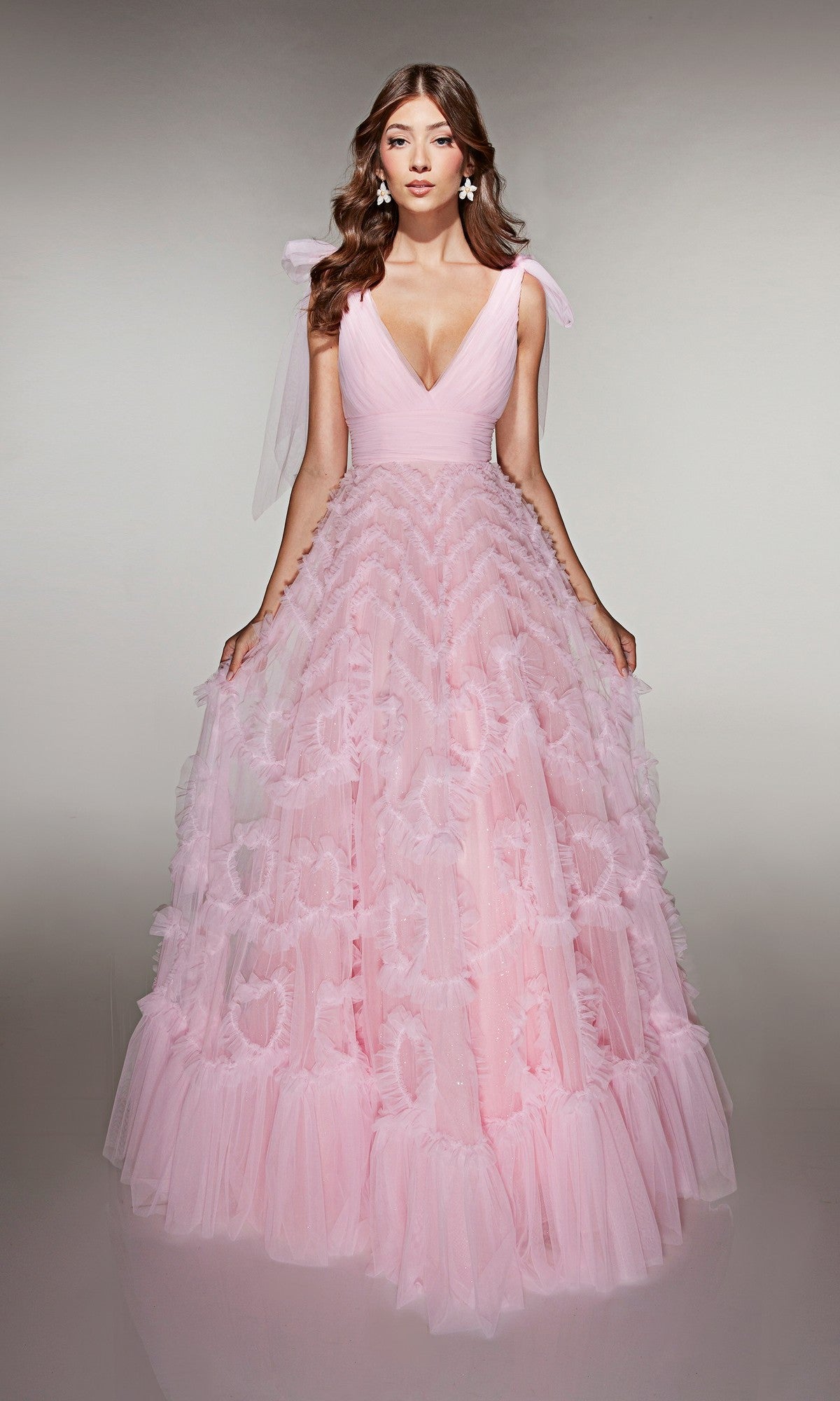 A woman stands facing forward in the Alyce 62079 long prom dress, a pale pink gown with a ruffled tulle A-line skirt, deep V-neckline, and delicate tulle details.