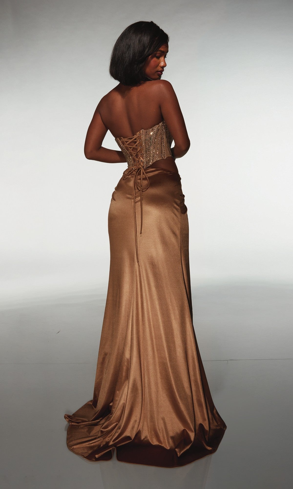 A woman faces away in the Alyce 62087 long prom dress—strapless, with a sweetheart neckline, corset-style bronze satin bodice, lace-up back, and a flowing skirt.