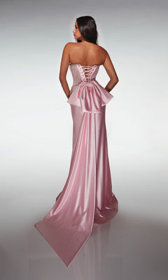 Woman wearing the Alyce 62089 long prom dress, a pink satin strapless gown with a fitted lace corset bodice, lace-up back, large bow detail, and long train, standing against a plain light background.