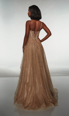 A woman faces away, wearing the Alyce 62093 long prom dress—a floor-length gold glitter tulle gown with thin straps and a lace-up back—set against a plain light background.