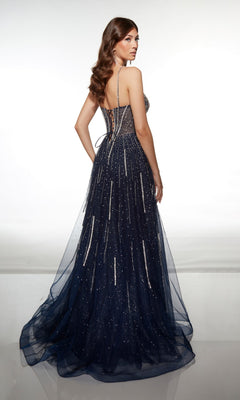 A woman stands facing away, wearing the Alyce 62093 long prom dress—a dark blue glitter tulle gown with thin straps, lace-up back, and a floor-length sparkling finish.