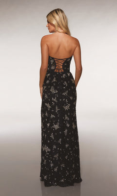 A woman models the Alyce 62098 long prom dress, featuring black sequins and a lace-up back, standing with her back to the camera.