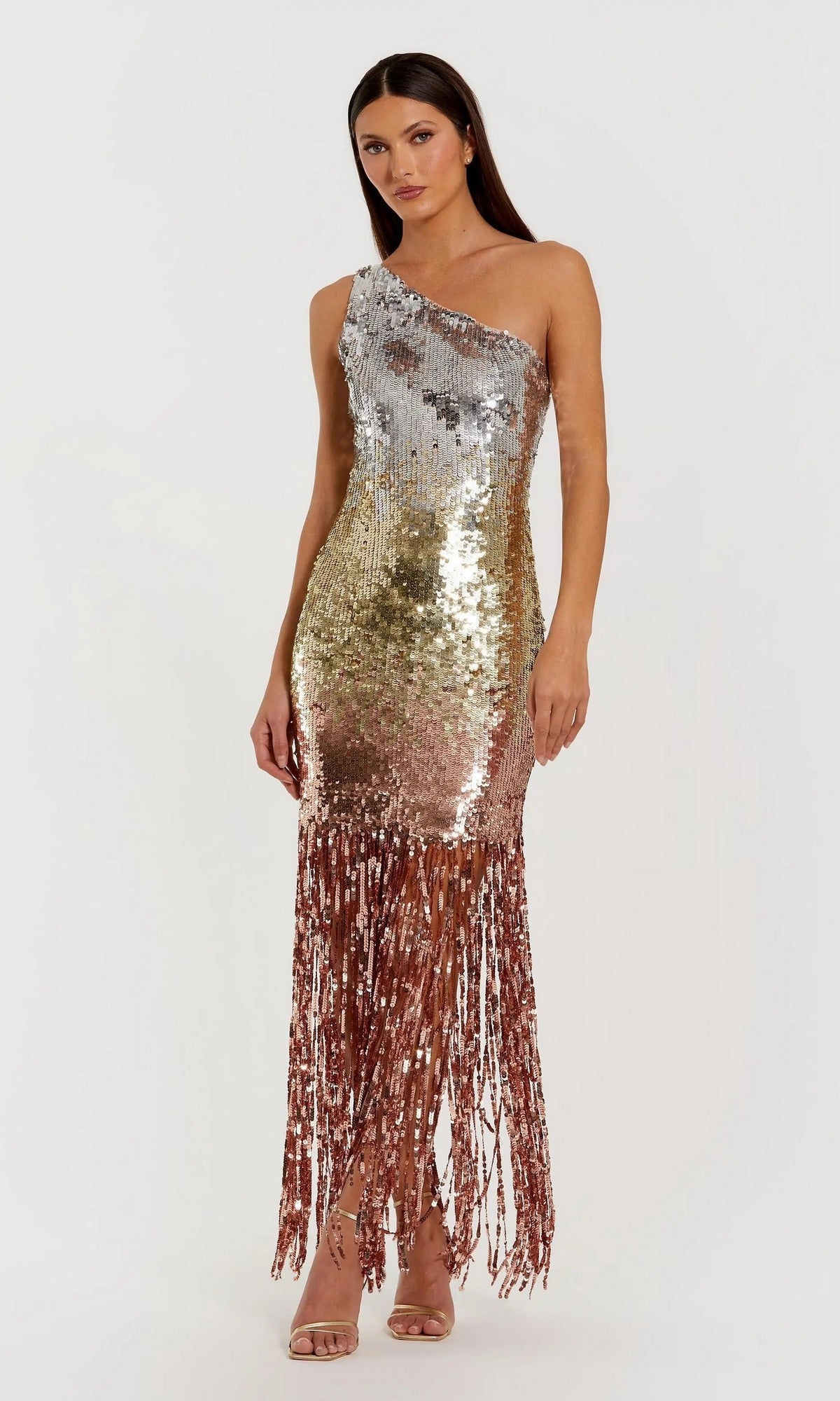 A woman wears the Mac Duggal 6212 long formal dress, a one-shoulder gown in metallic gold and silver ombre sequins with fringe at the hem, paired with strappy heels.