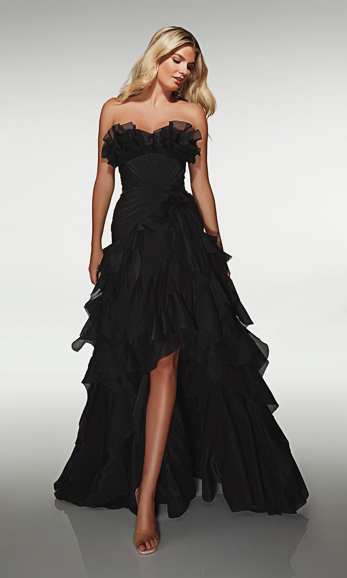 A woman wearing the Alyce 62124 Long Prom Dress in black, featuring a strapless crinkle organza design with a ruffled high-low hemline, stands against a plain light background.