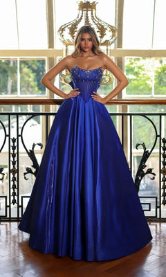 A woman stands indoors in front of large windows wearing the Alyce 62134, a royal Long Prom Dress featuring shimmering embellishments on the bodice and a floor-length strapless silhouette for a stunning look.