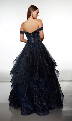 A woman stands facing away in the Alyce 62173 long formal dress, an off-the-shoulder dark blue ball gown with a lace-up back and layered glittery tulle.