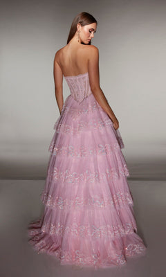 A woman faces away from the camera in the Alyce 62191 long prom dress, showcasing a strapless embellished corset bodice and tiered pink A-line skirt with lace and sequin details against a plain background.