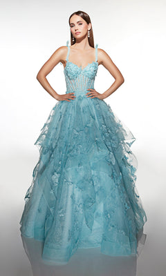 A woman stands gracefully against a plain backdrop wearing the Alyce 62199 long prom dress—a light blue gown with a corset bodice, tulle ballgown skirt, floral appliqués, and delicate spaghetti straps.