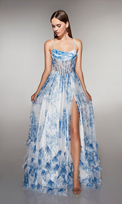A woman wears the Alyce 62202 long prom dress, featuring a blue and white floral print, high slit, and sheer corset bodice, standing against a plain background.